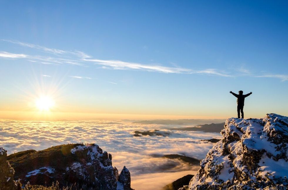 Man celebrates success as he reaches the top of a mountain
