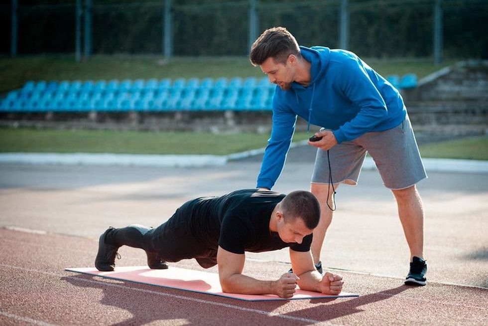 Man doing plank exercise and workout with personal fitness trainer outdoor