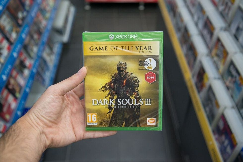 Man holding Dark Souls 3 Game of the Year edition videogame on Microsoft XBOX One console in store.