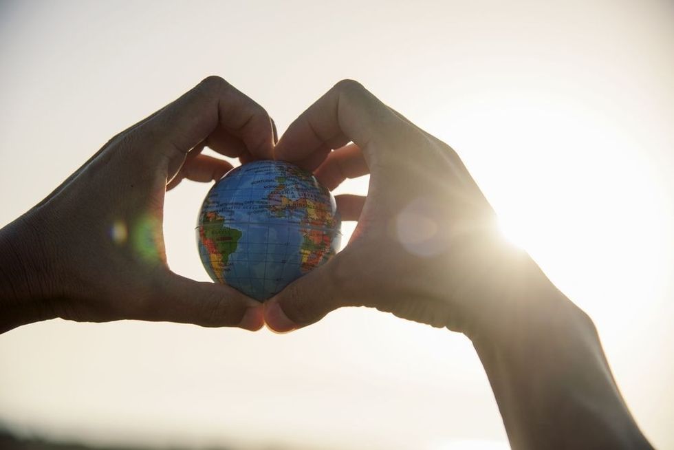 Man with a world globe in his hands forming a heart against the sky