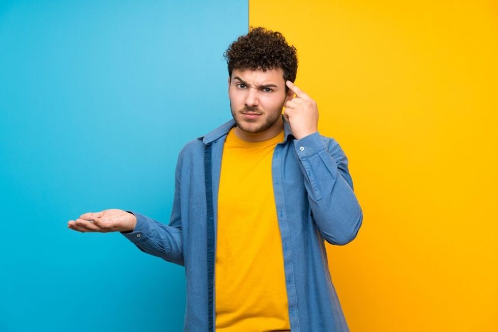 Man with curly hair over colorful wall making the gesture of madness putting finger on the head