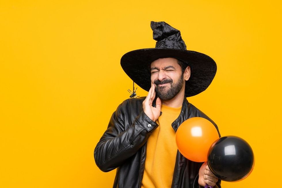 Man with witch hat holding black and orange air balloons for halloween party with toothache