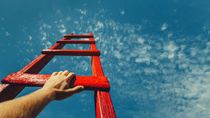 Mans Hand Reaching For Red Ladder Leading To A Blue Sky