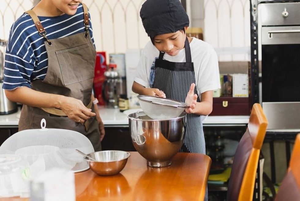 Mother and son sieving flour into a bowl for baking in kitchen.