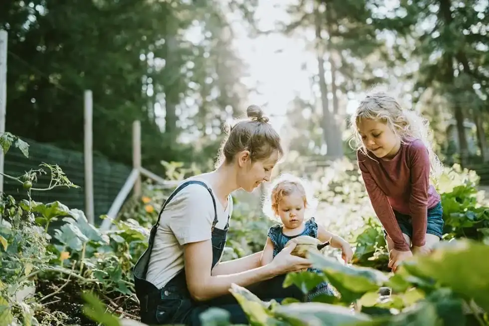 Mother showing her two daughters how to plant seeds in the garden.