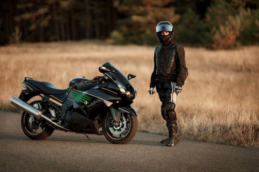 Motorcycle driver in a helmet and leather jacket stands on the road next to a sports motorcycle.