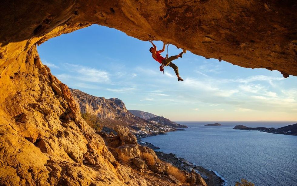 Mountain climber on overhanging rock against beautiful view of coast below