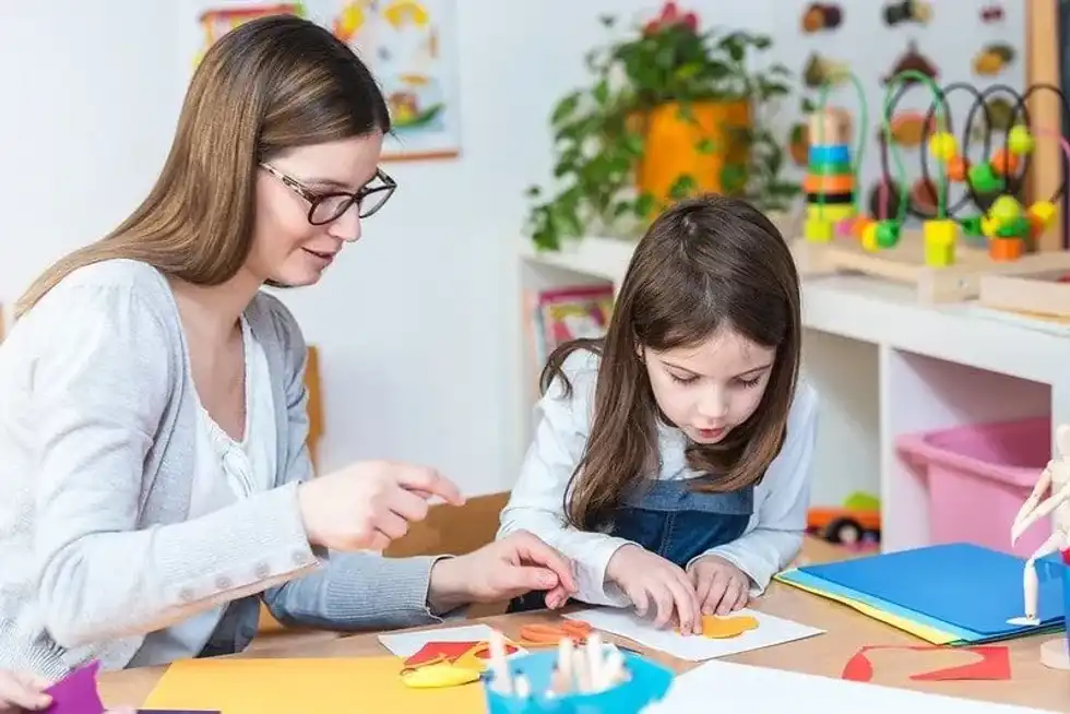 Mum and daughter sat at the table doing arts and crafts with paper, making origami.