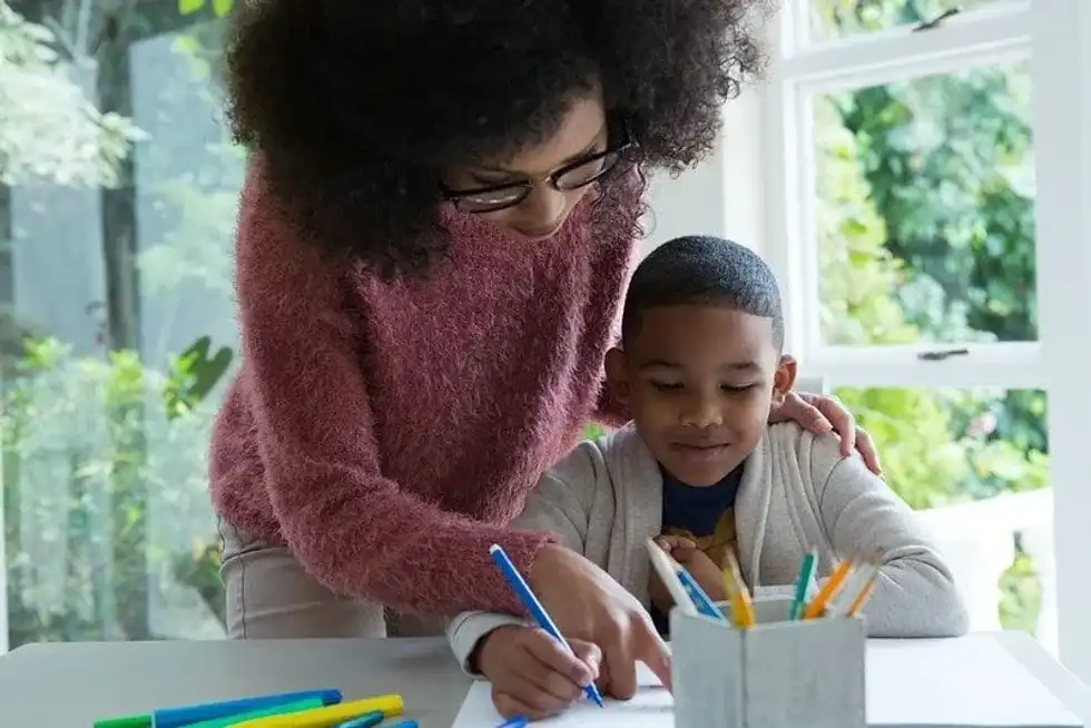Mum helping her son who is sat at the table learning about Iron Age Weapons.