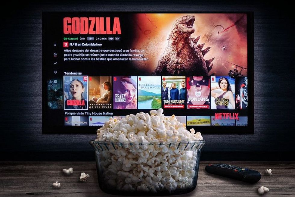 Netflix app on tv screen playing "Godzilla" behind a bowl of popcorn and a remote control.