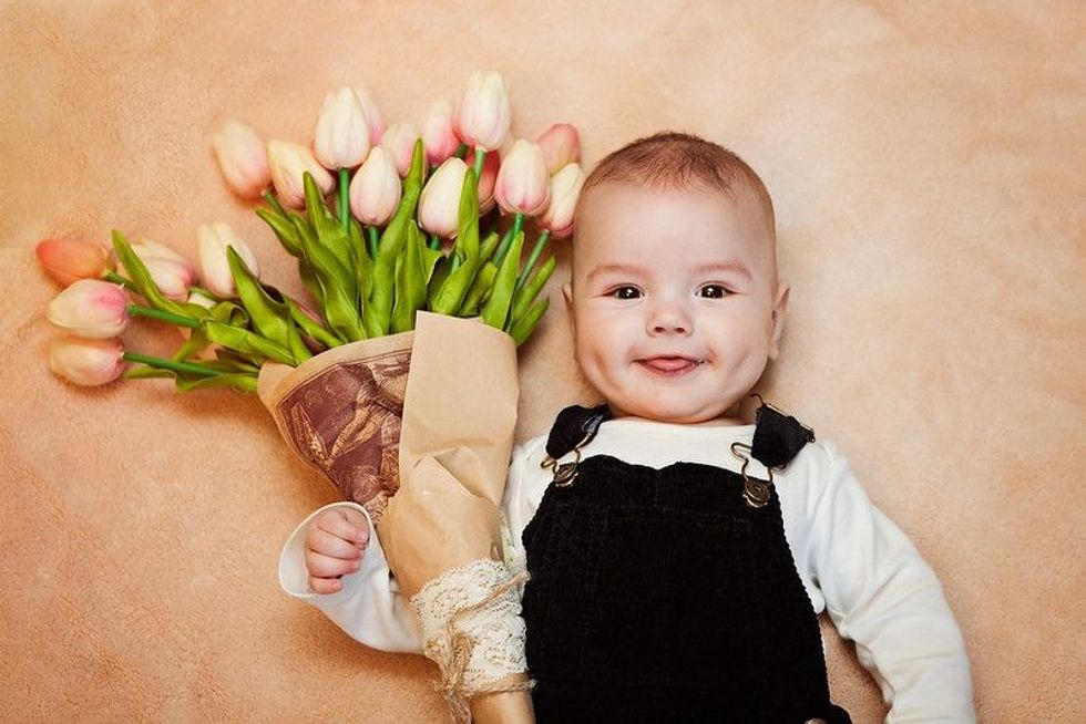 Newborn baby boy holding orange pastel tulip bouquet.