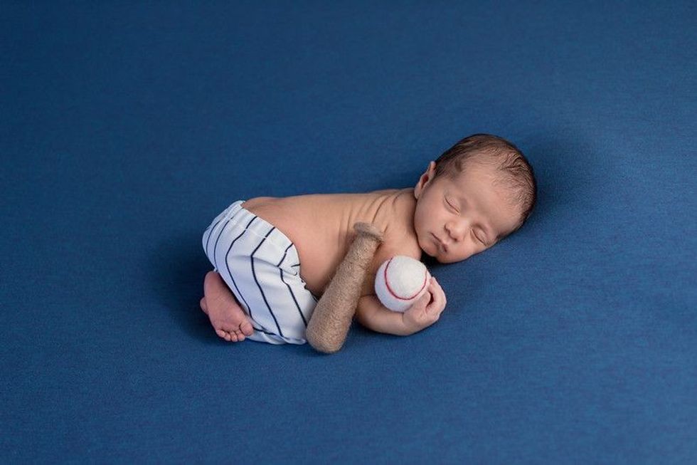 Newborn baby dressed as baseball player with bat and ball sleeping