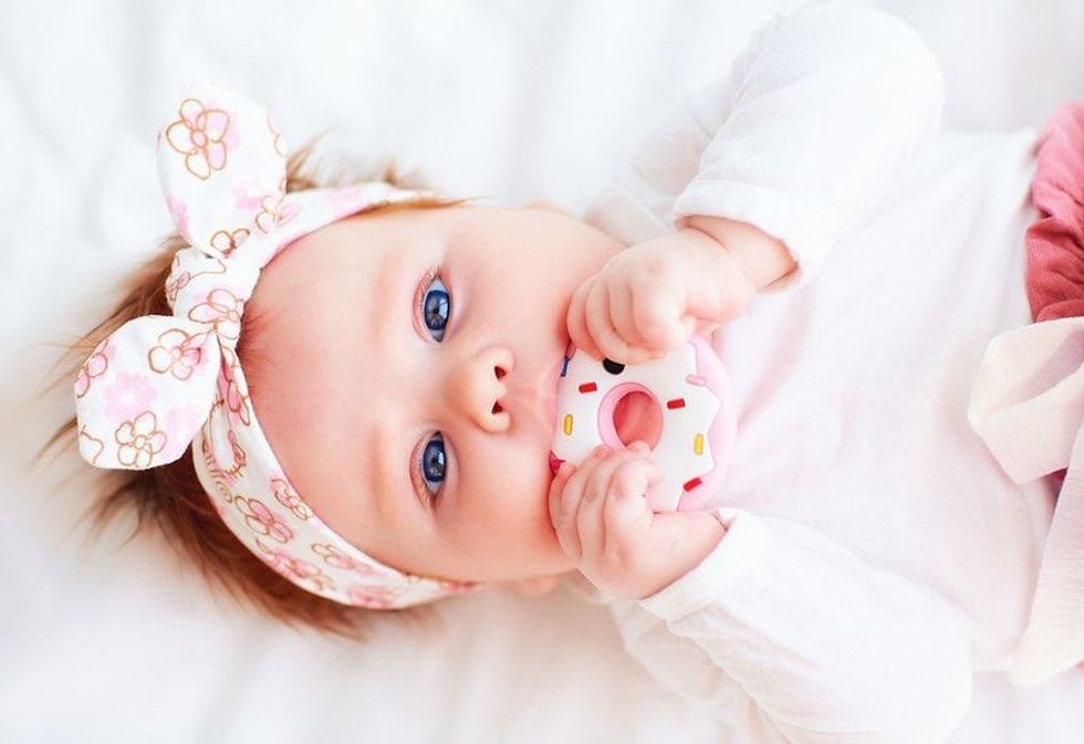 Newborn baby girl nibbling on a donut teether.