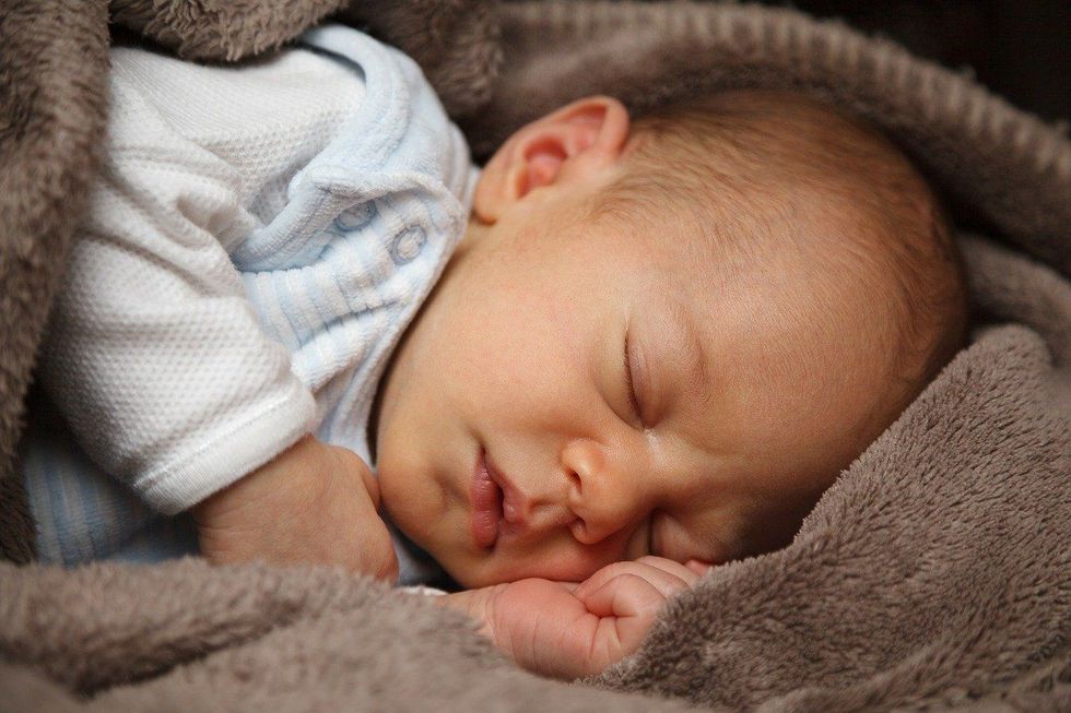 Newborn baby sleeping peacefully in a gray blanket.