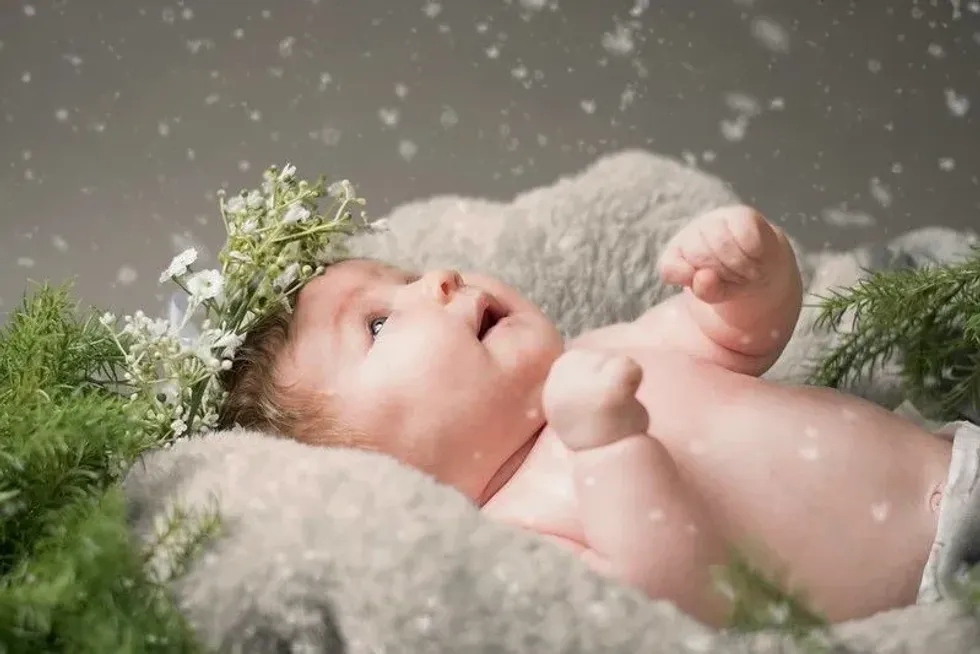 Newborn baby wearing floral crown is amazed by snowfall