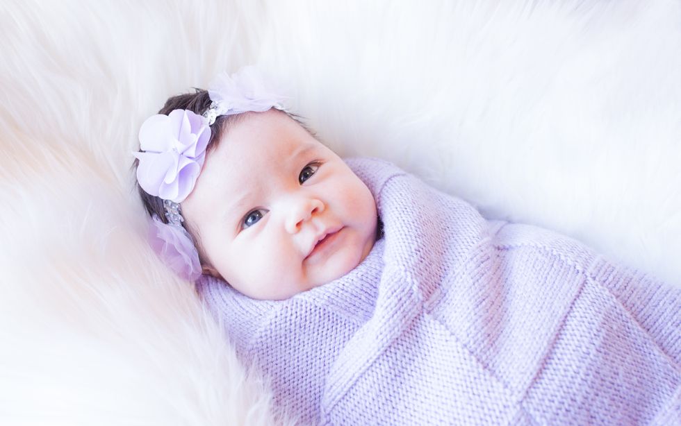 Newborn cute baby girl wrapped in a purple shawl wrap
