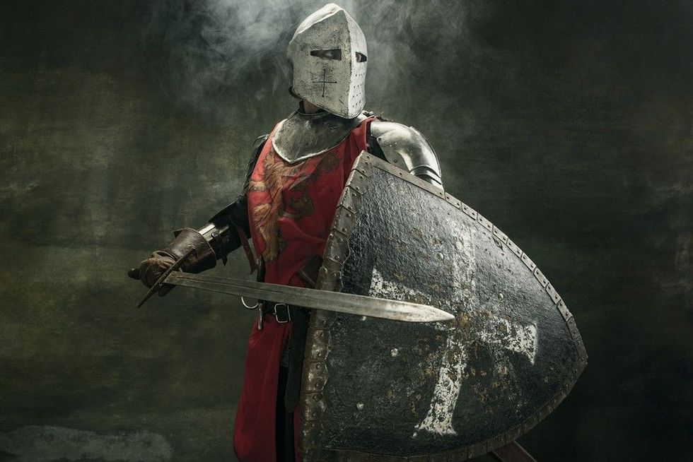 Noble warrior. Portrait of one medeival warrior or knight in armor and helmet with shield and sword posing isolated over dark background.
