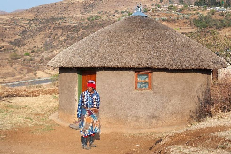 Old Basotho woman standing in front of her traditional house.