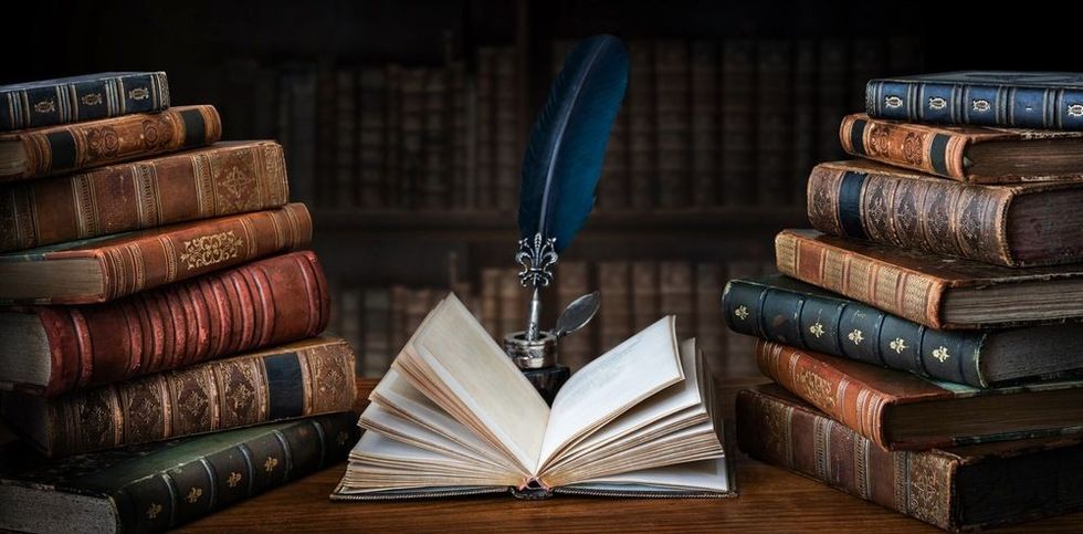 Old books ,quill pen and vintage inkwell on wooden desk in old library.