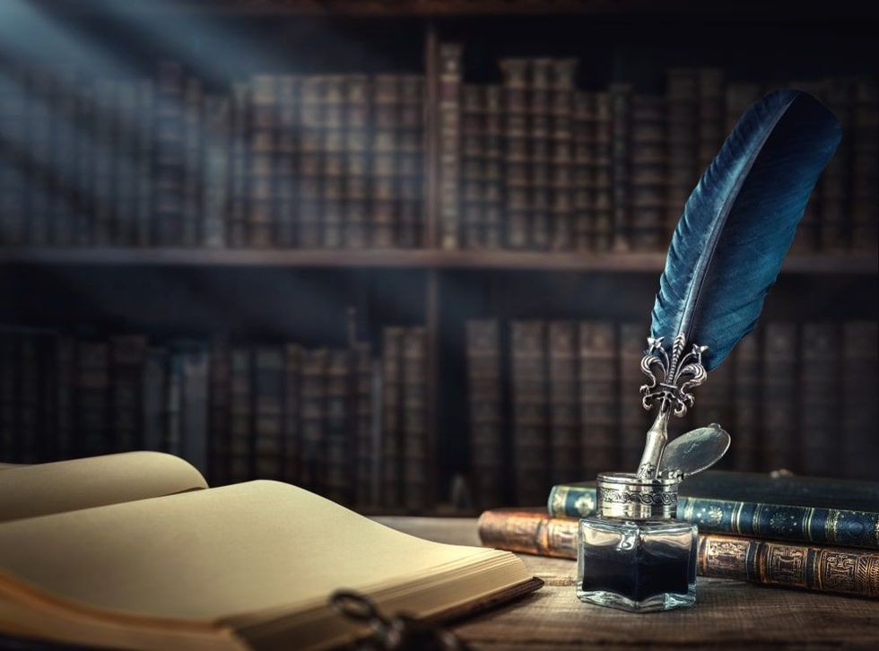 Old quill pen, books and vintage inkwell on wooden desk
