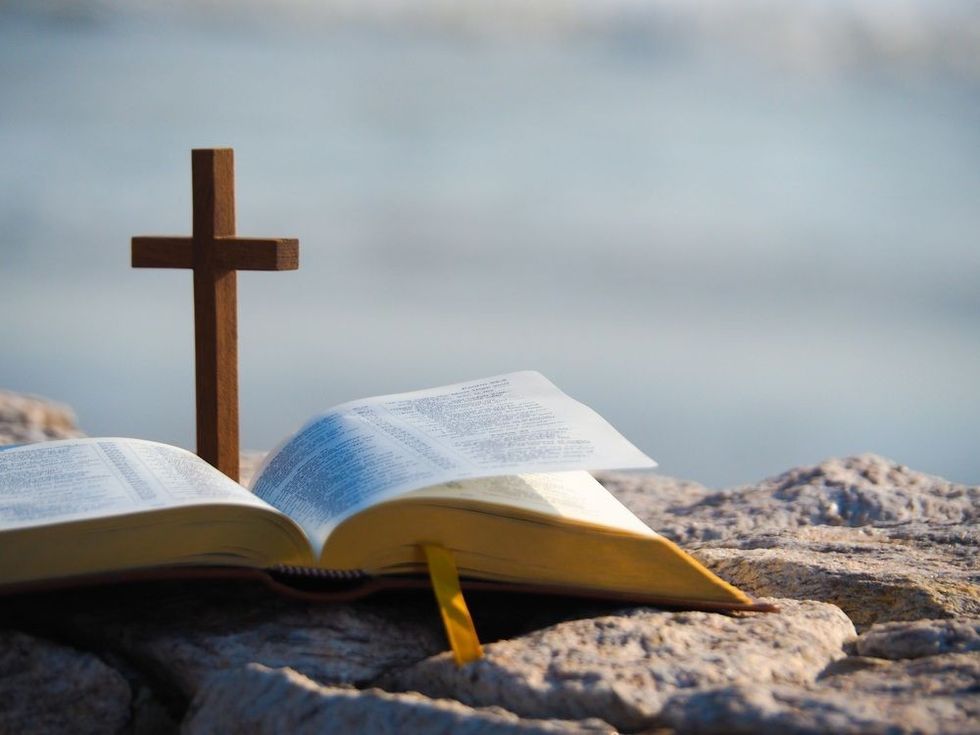 Open bible and wood holy cross with blue sea as background. 
