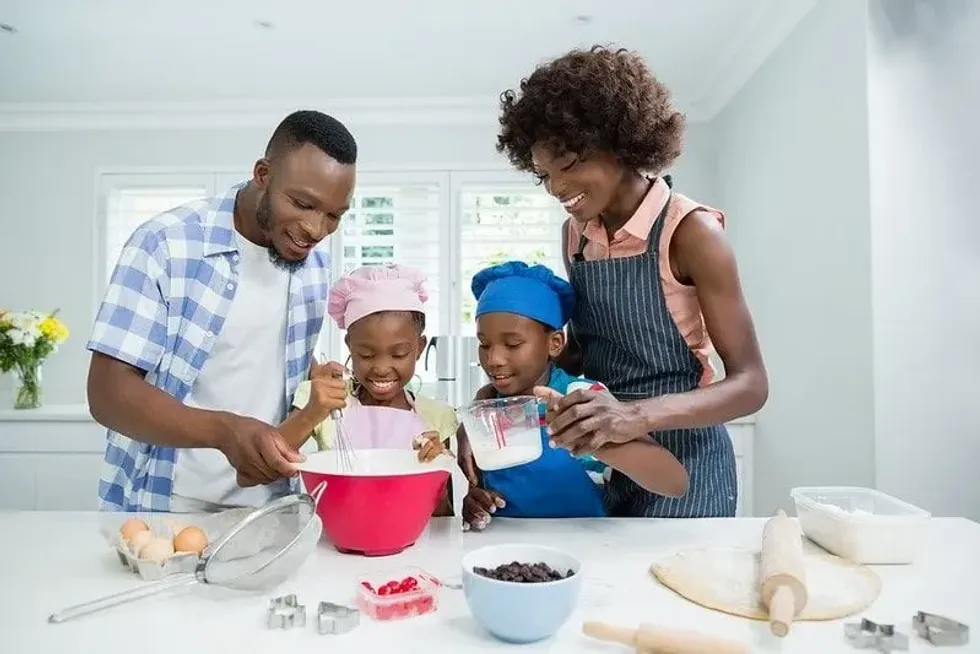 Parents and their two children in the kitchen baking a football cake together.