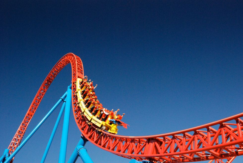  Passengers on a red roller coaster are reaching the peak of a steep track against a clear blue sky.
