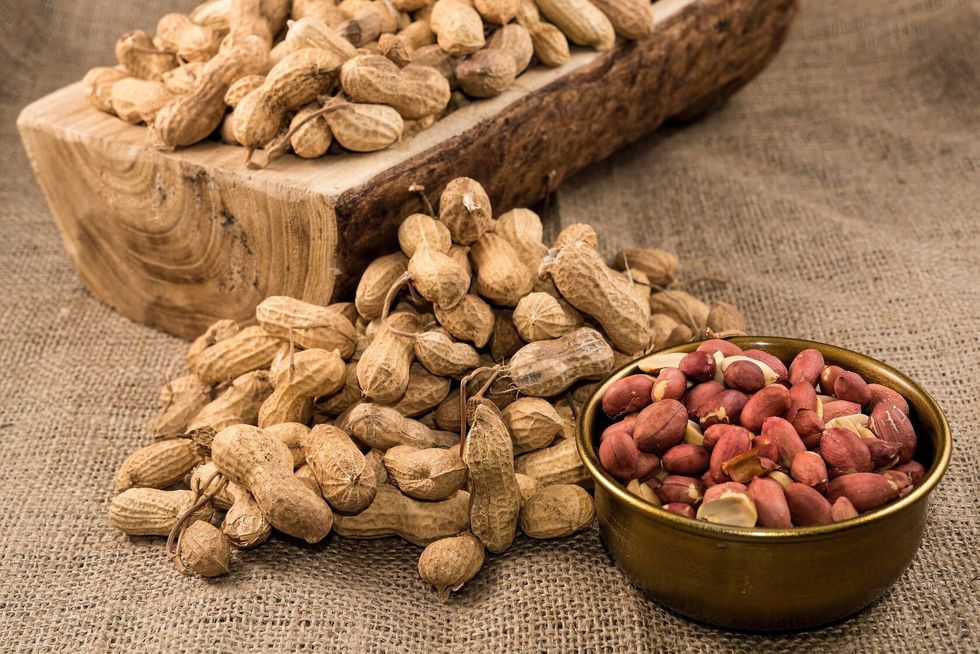 Peanuts in nutshell on a piece of wood and peeled peanuts in golden bowl on sackcloth
