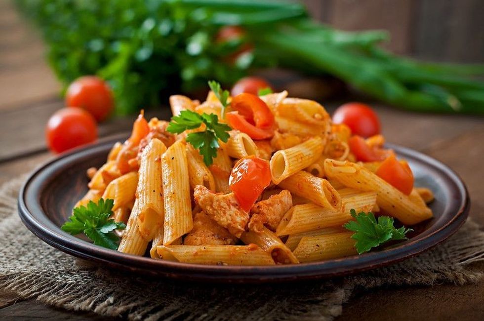 Penne pasta in tomato sauce with chicken, tomatoes decorated with parsley on a wooden table