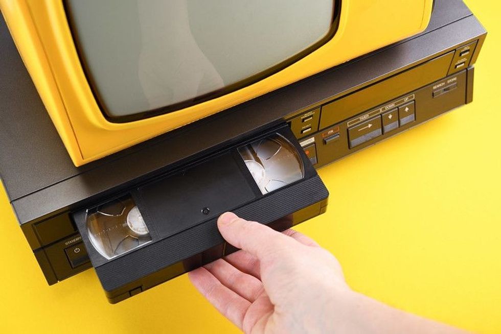 Person inserting VHS videocassette in the video recorder to watch the video on tv