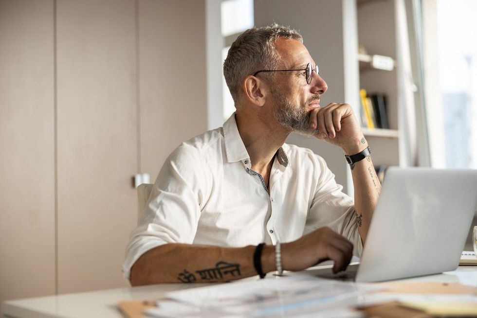 Philosophical person propping up his chin with a hand and getting distracted from working process with something outside.