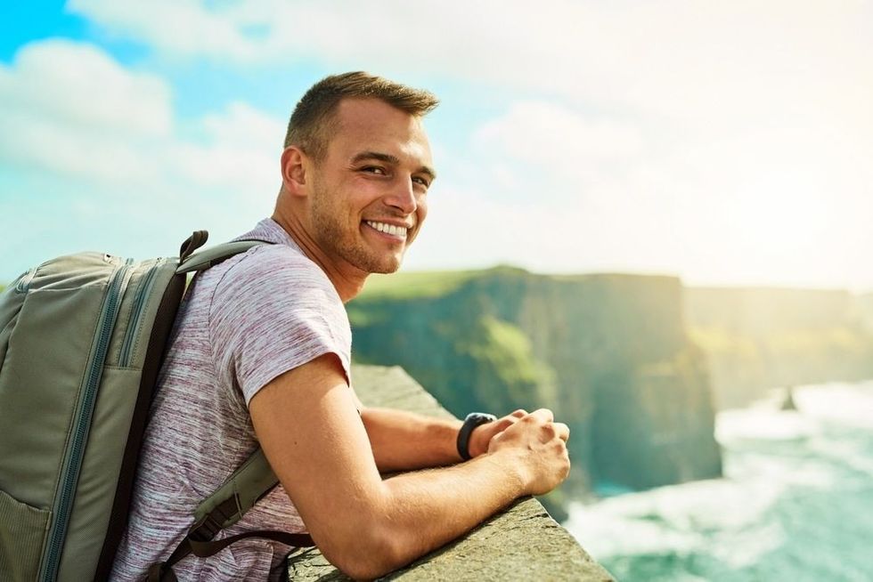 Photo of a man smiling while resting his hands on the edge of a cliff