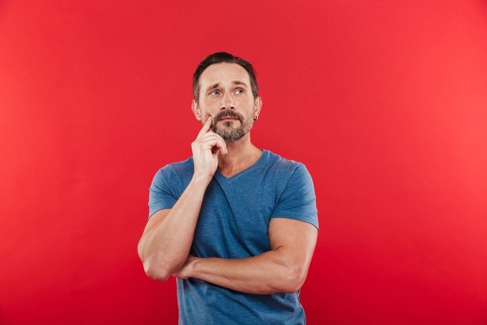Photo of man 30s wih brooding gaze in casual t-shirt looking upward and thinking or remembering isolated over red background.