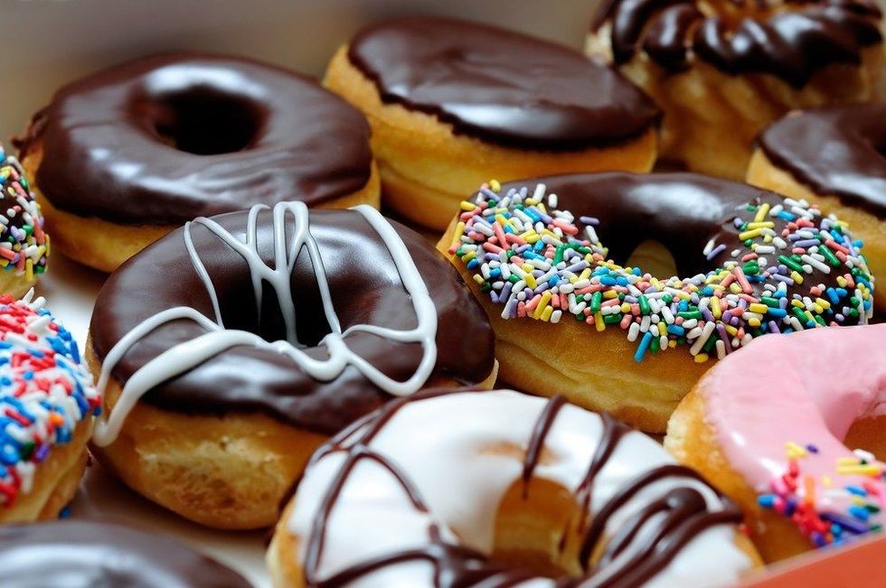 Picture of assorted donuts in a box with chocolate frosted, pink glazed and sprinkles donuts.