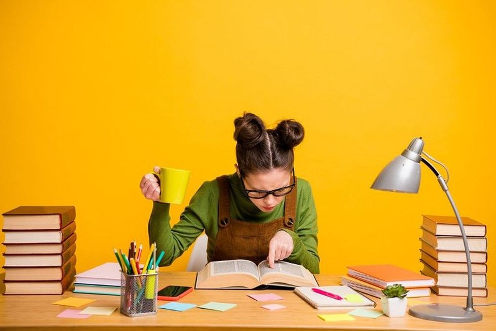 Portrait of a girl focused knowledgeable brainy diligent woman nerd reading book finding solution drinking caffeine isolated bright vivid shine vibrant yellow color background