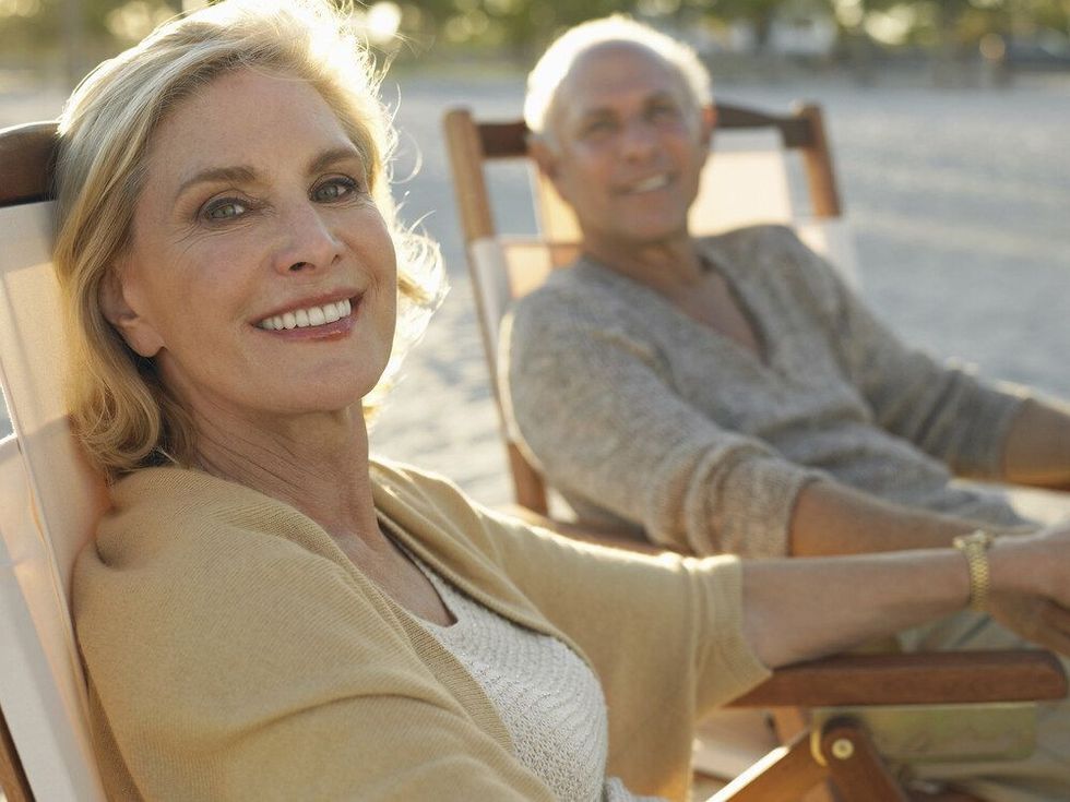 Portrait of happy middle age woman with man relaxing on deckchairs at beach
