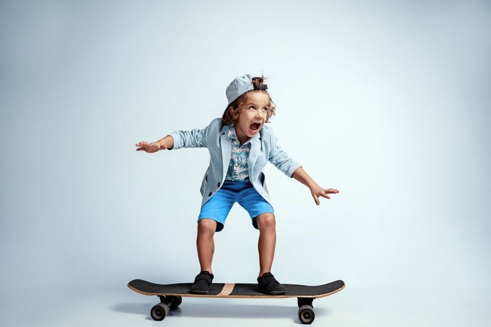Pretty young boy on skateboard in casual clothes on white studio background.