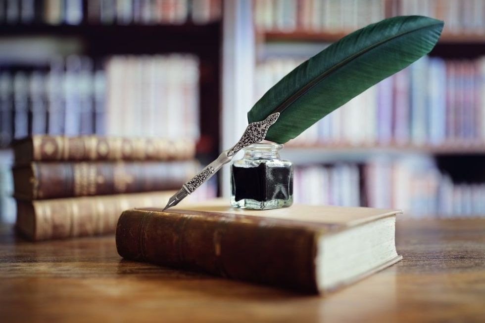 Quill pen and ink well resting on an old book in a library concept for literature
