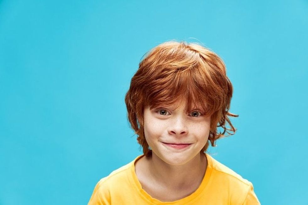 Red-haired child in a yellow T-shirt on a blue background.