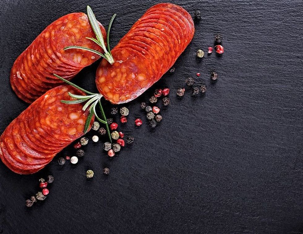 Sausage or salami with fresh herbs colorful seasoning on black stone.