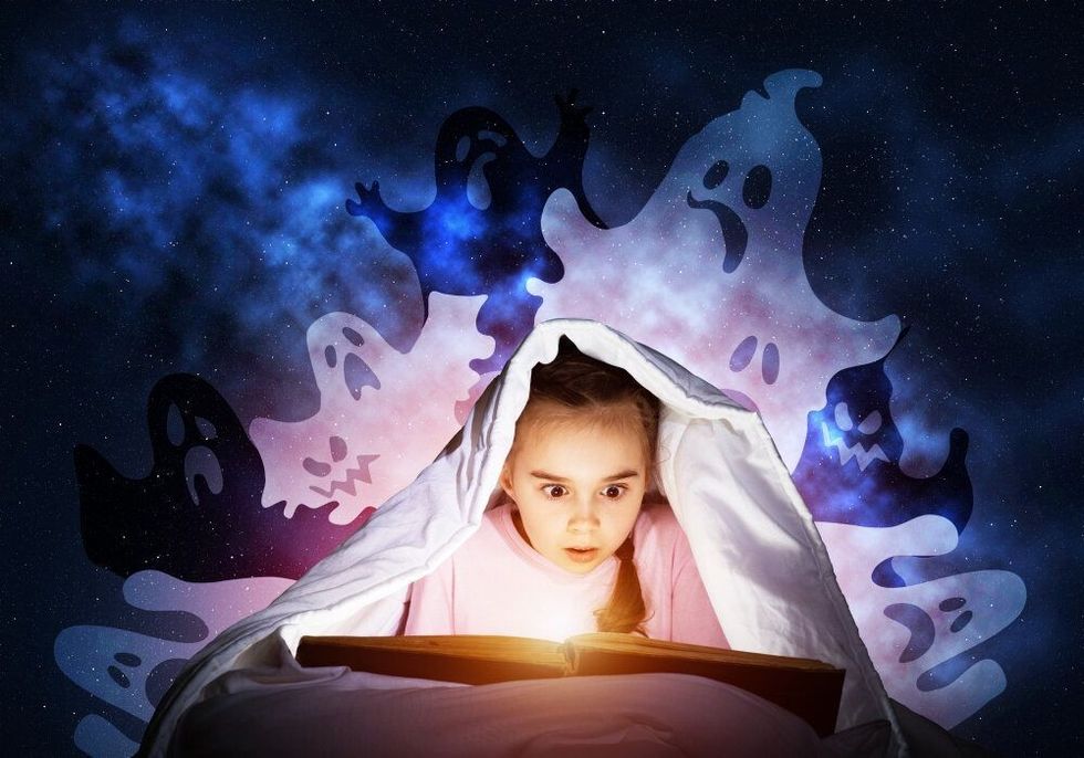 Scared little girl reading ghost book in bed