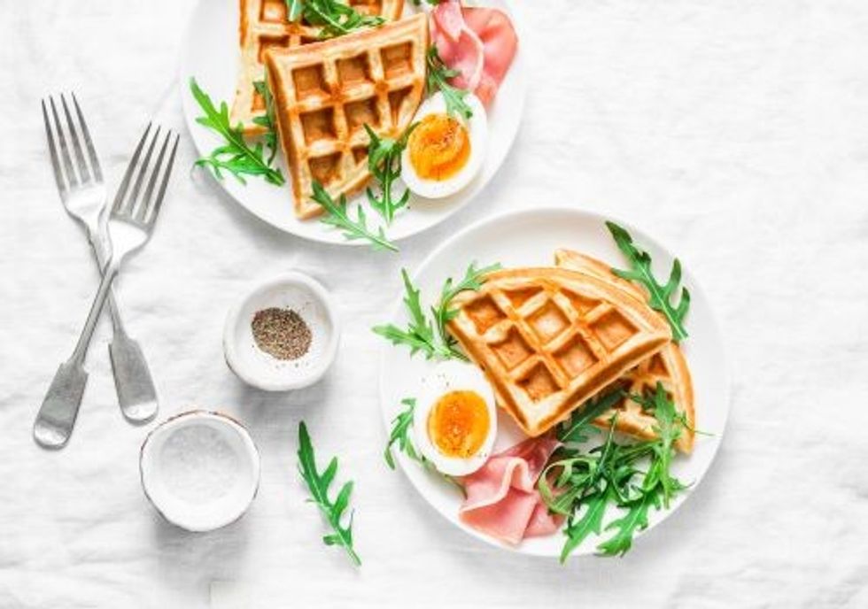 Served brunch with potatoes savory waffles, boiled egg, ham and arugula on light background, top view.