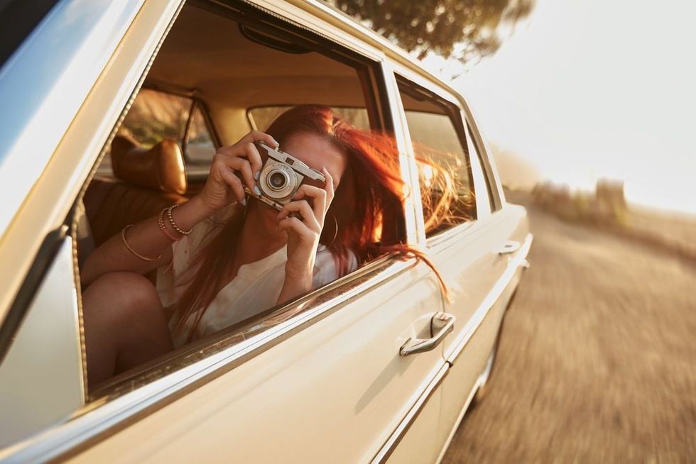 Shot of young woman taking photos while sitting in a car.
