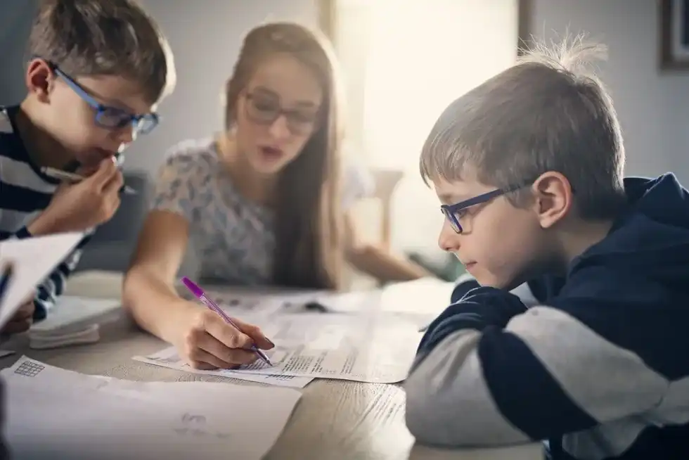 Sister sat at the table teaching her two younger brothers about the industrial revolution.