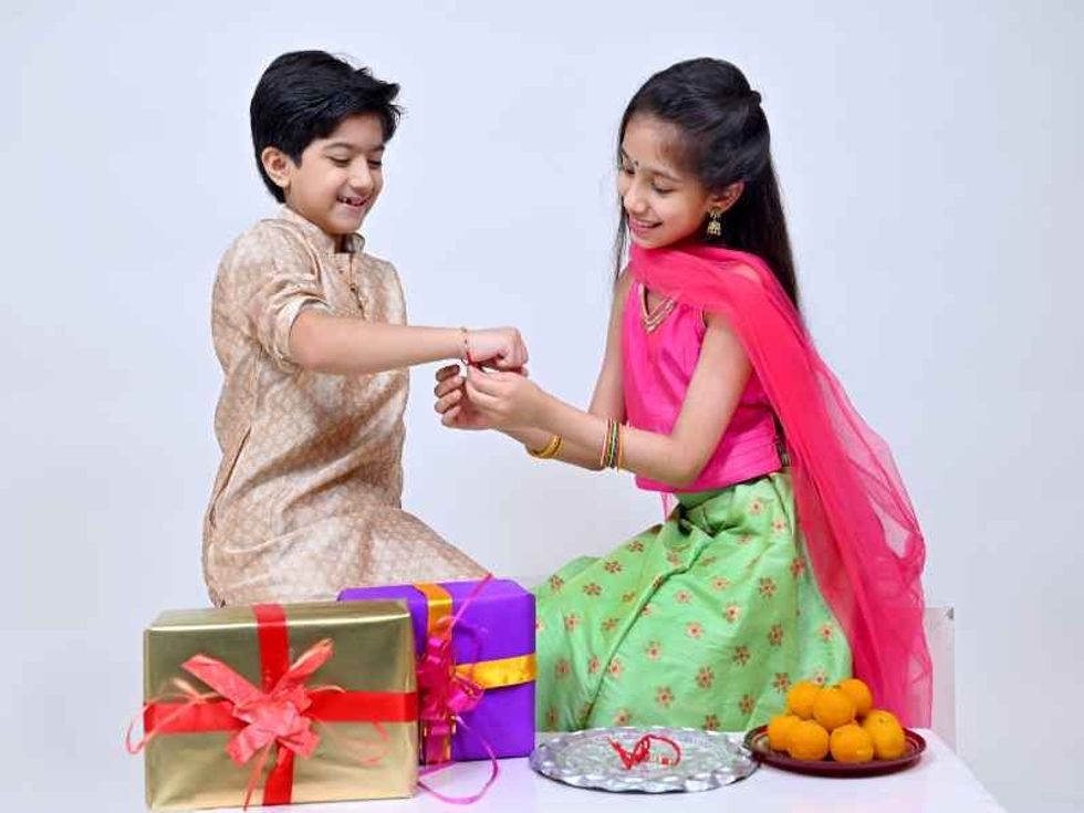 Sister tying colorful rakhi on her brother’s hand with brass dish full of puja accessories