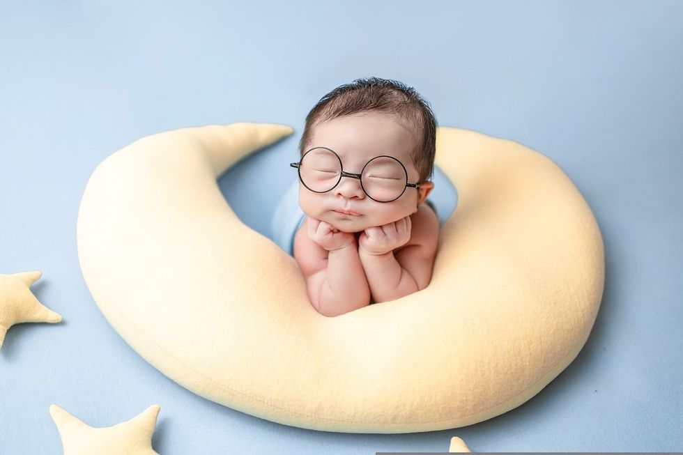 sleeping newborn baby with an eyeglass and jaw placed on folded hands