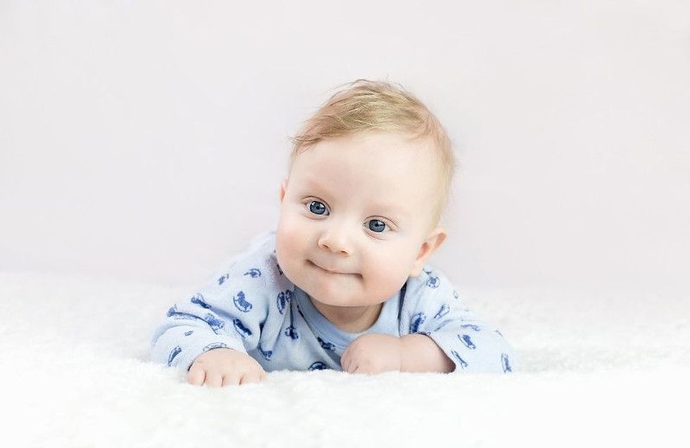 Smiling baby boy with blue eyes lying on his stomach.