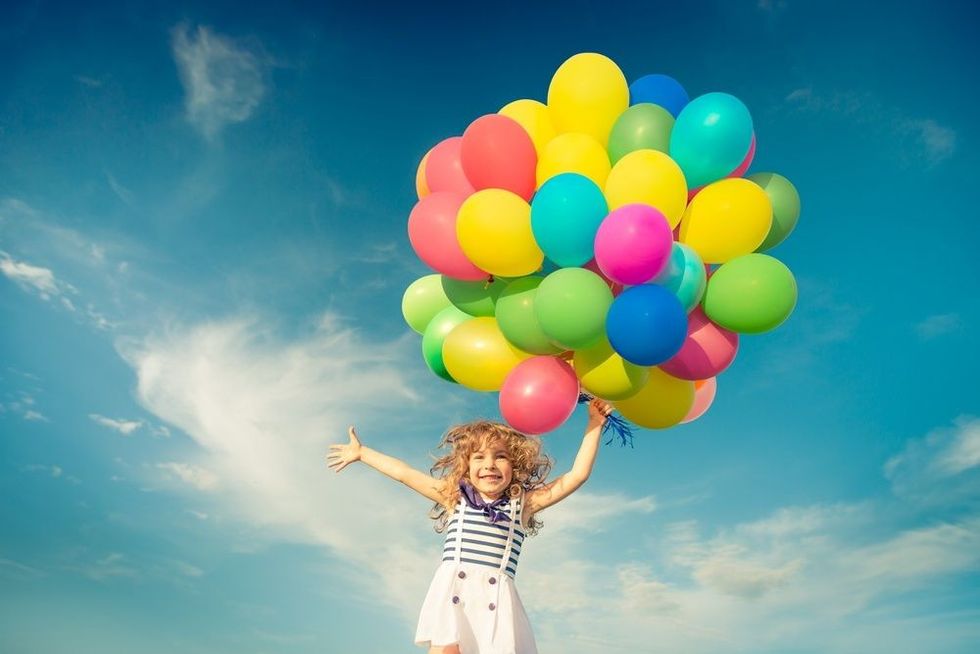 Smiling kid having fun in green spring field against blue sky background.