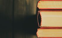 Spine of books with scarlet covers on a wooden background.