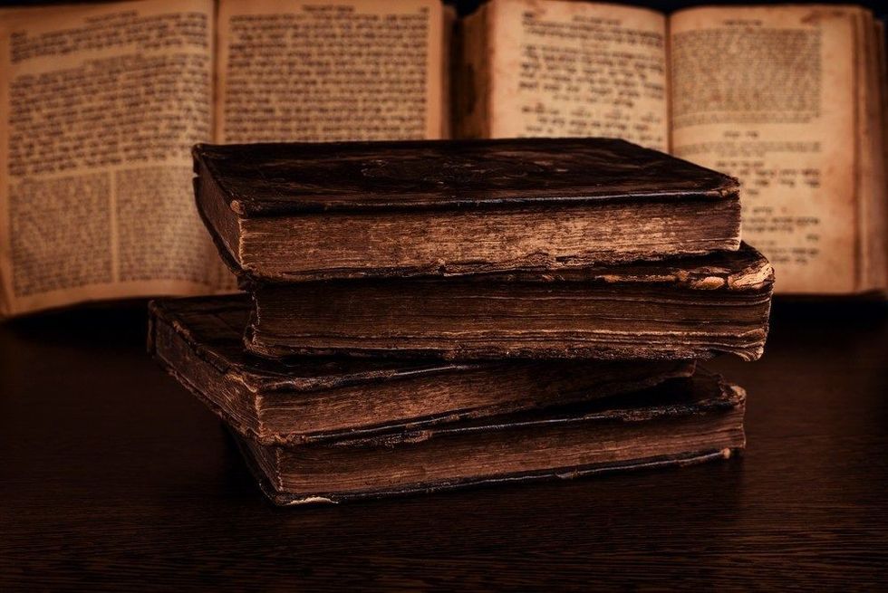 Stack of old worn shabby jewish books in leather binding and open blurred Torah in the background in the dark. 